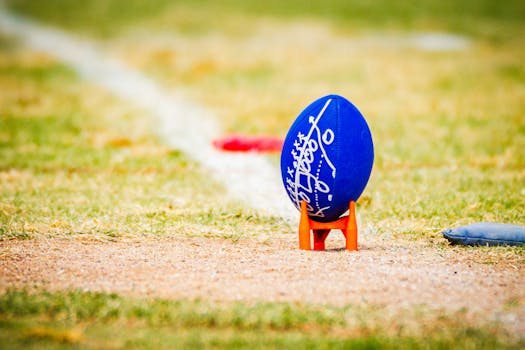 Blue American football on tee, ready for kickoff on a grassy field.