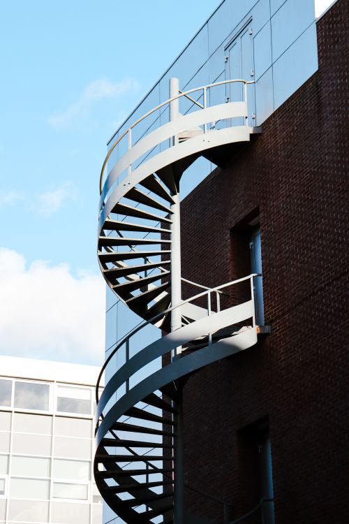 Free Exterior spiral staircase on building against a bright blue sky, showcasing architecture contrast. Stock Photo