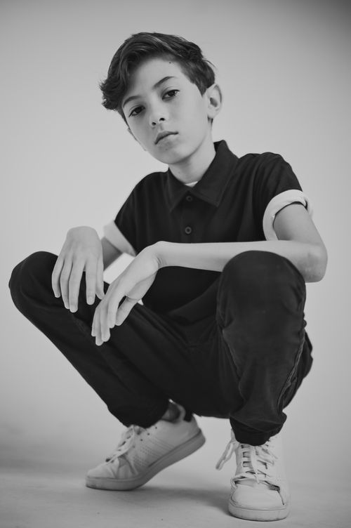 Free Artistic black and white portrait of a fashionable teenager in casual attire squatting confidently. Stock Photo