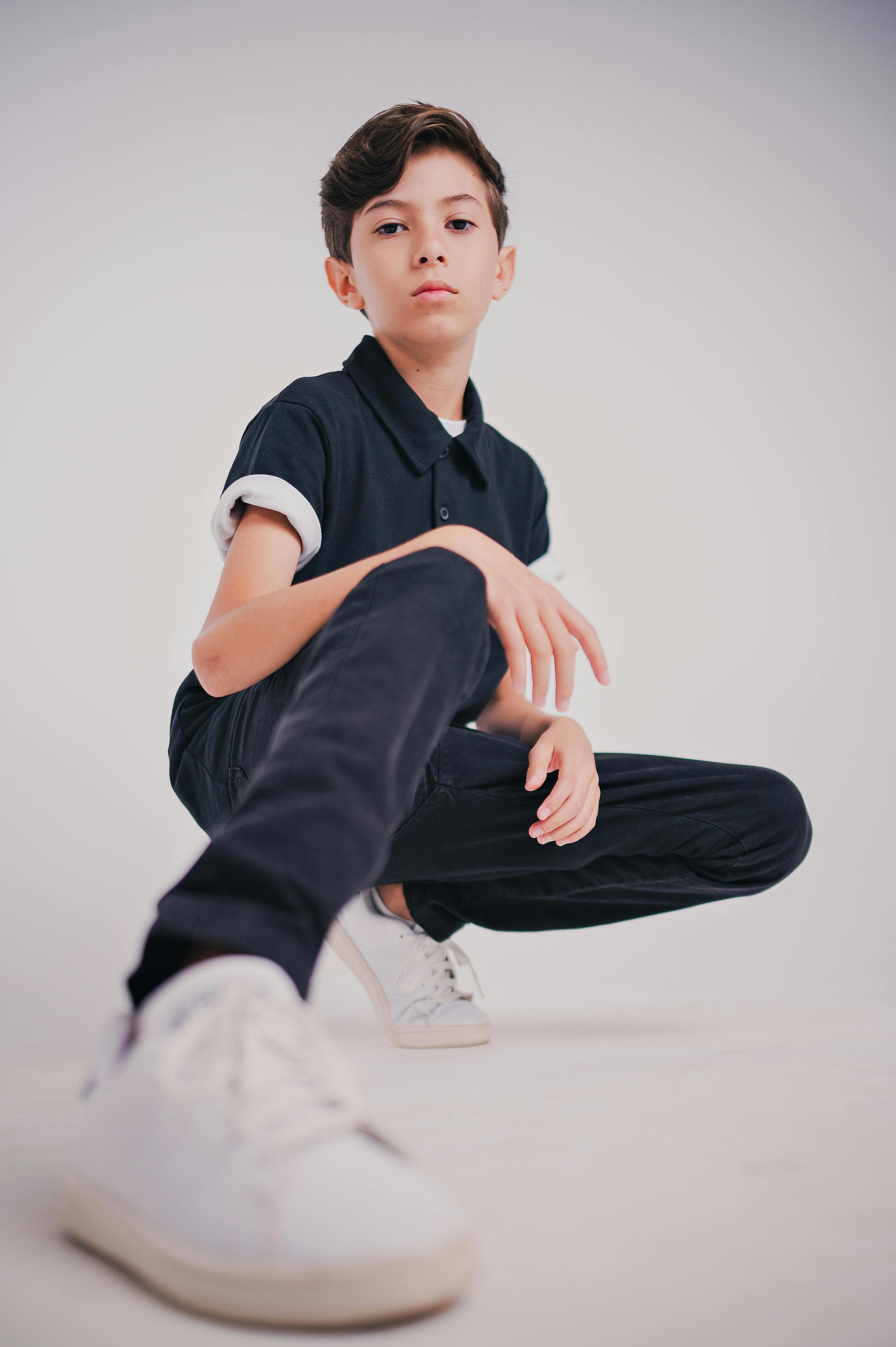 Confident young boy striking a pose in casual attire with focus on white sneakers. Modern look.
