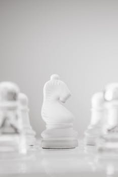 A minimalistic photo of a white chess knight in focus among blurred pawns, symbolizing strategy.