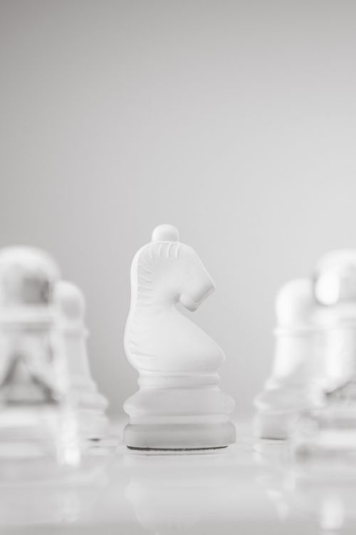 Free A minimalistic photo of a white chess knight in focus among blurred pawns, symbolizing strategy. Stock Photo