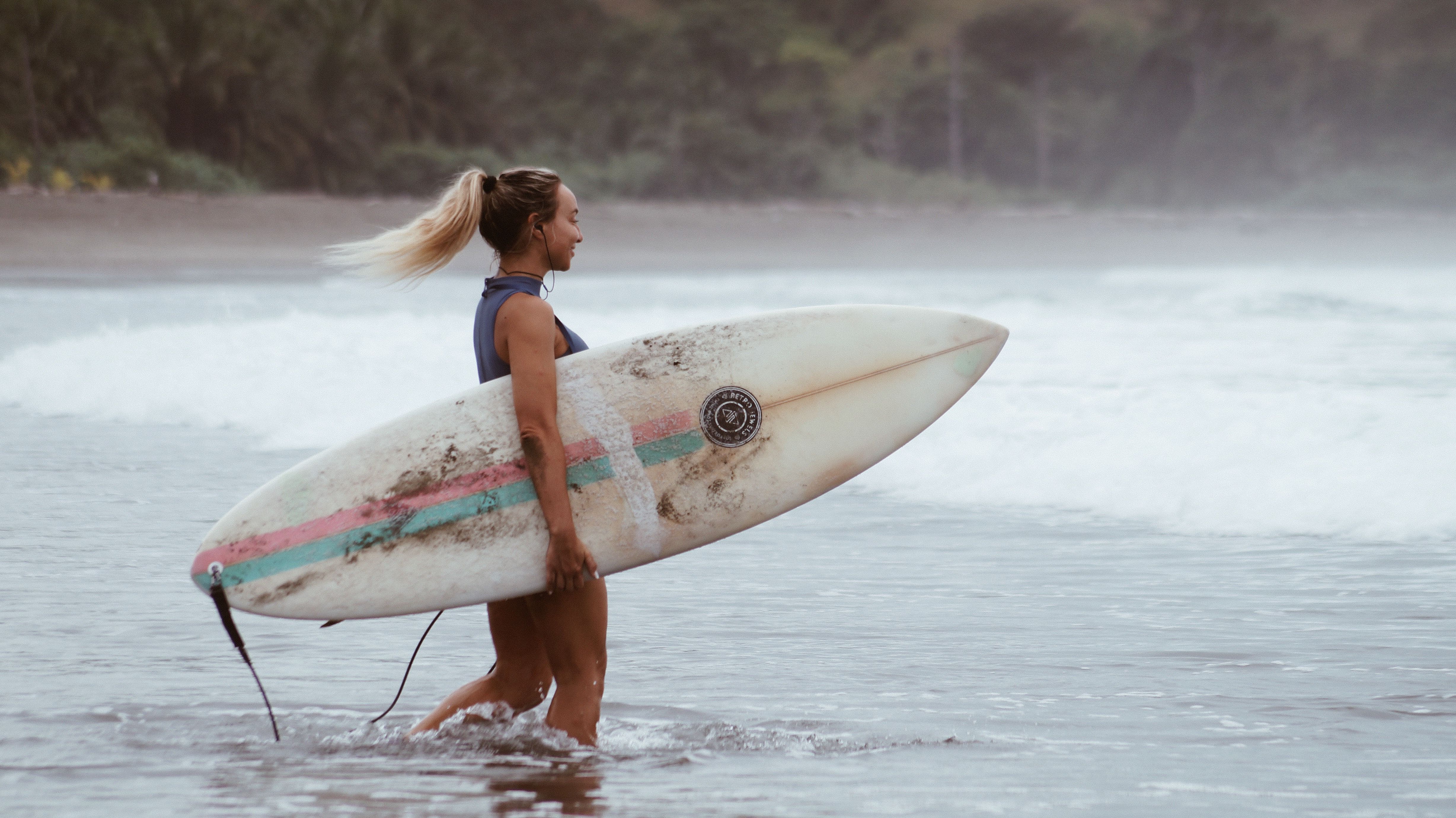 Woman carrying surfboard in the ocean, enjoying a warm, scenic beach.