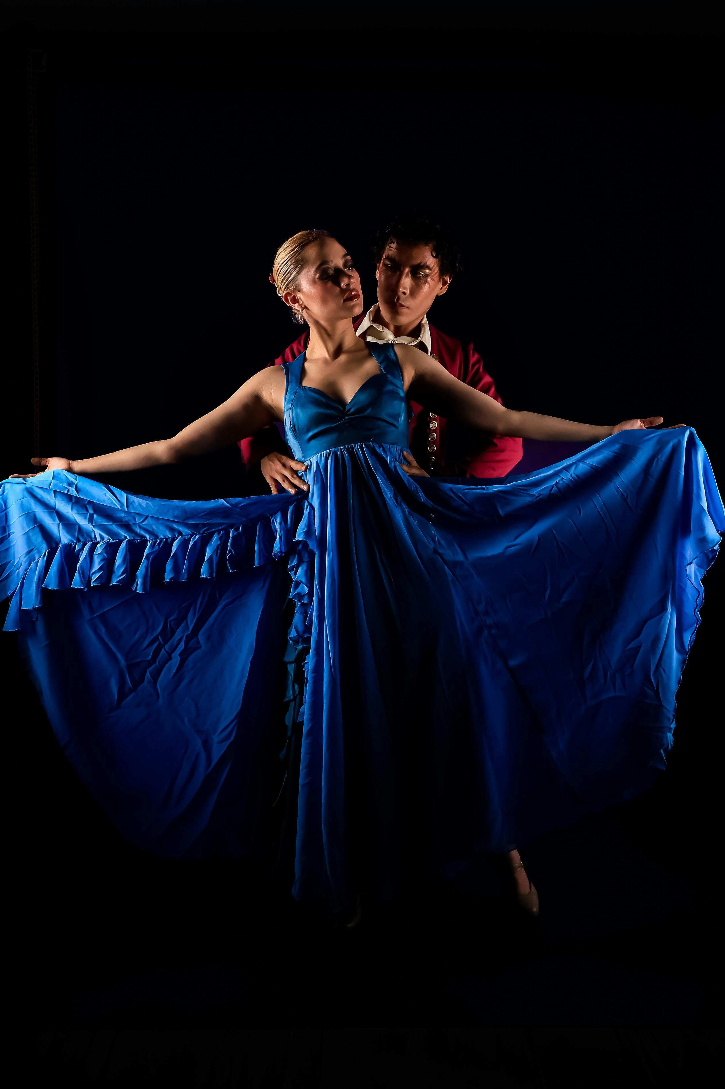 Ücretsiz Karanlık bir sahnede canlı mavi bir elbiseyle zarif bir balo dansı yapan bir çift. Stok Fotoğraflar