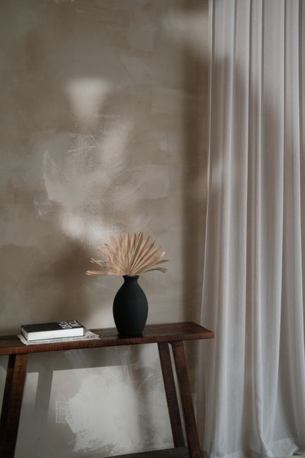 Cozy minimalist interior featuring a black vase with dry flowers on a console table against textured wall.