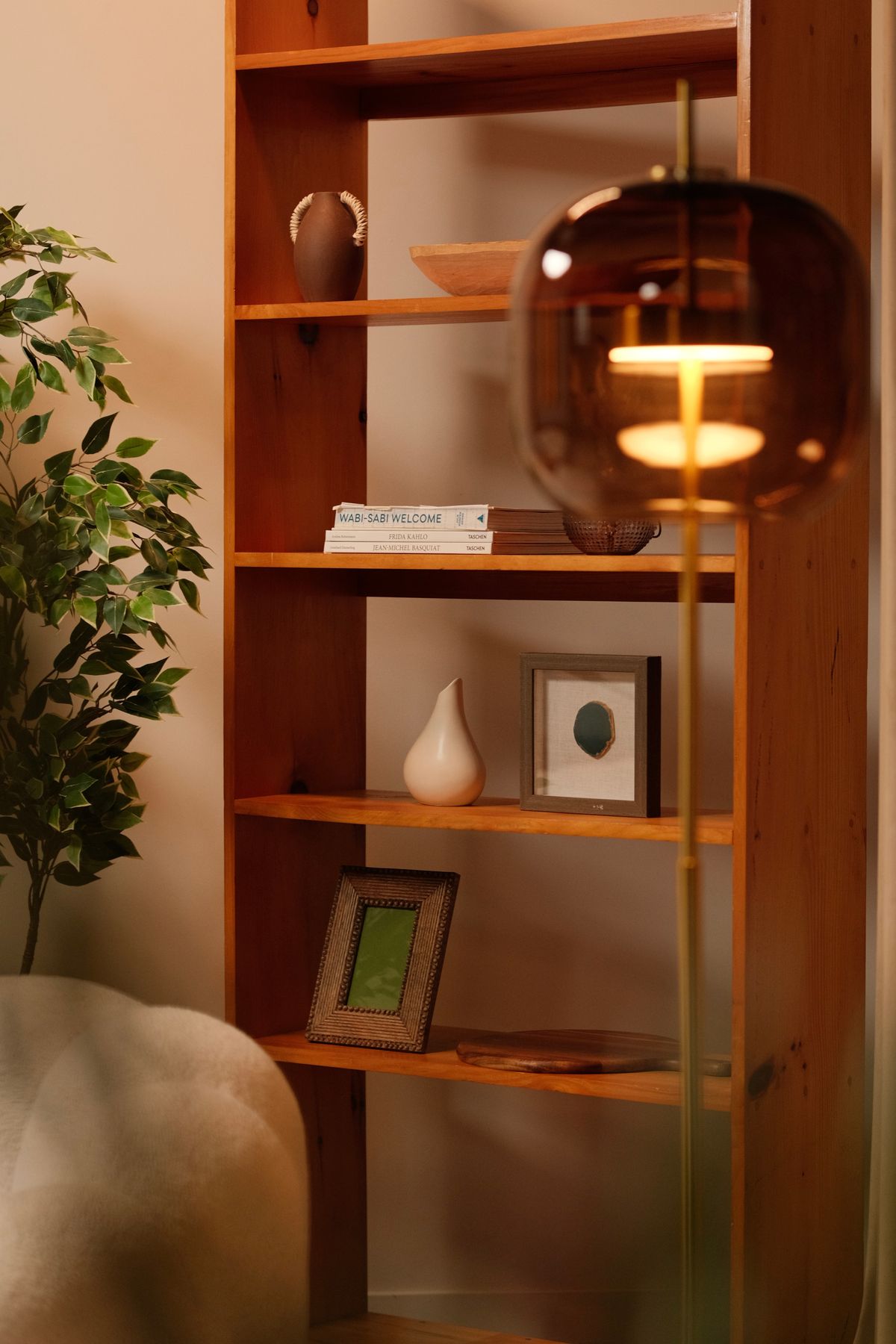 Warm minimalist living room featuring a wooden bookshelf and floor lamp. Illustrative editorial photograph.