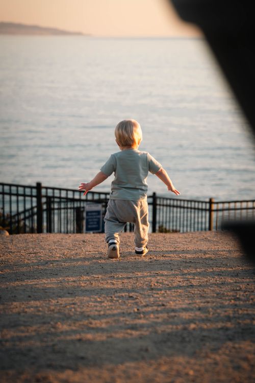 Free A toddler walks towards the ocean at Pismo Beach during sunset, capturing a serene and adventurous moment. Stock Photo