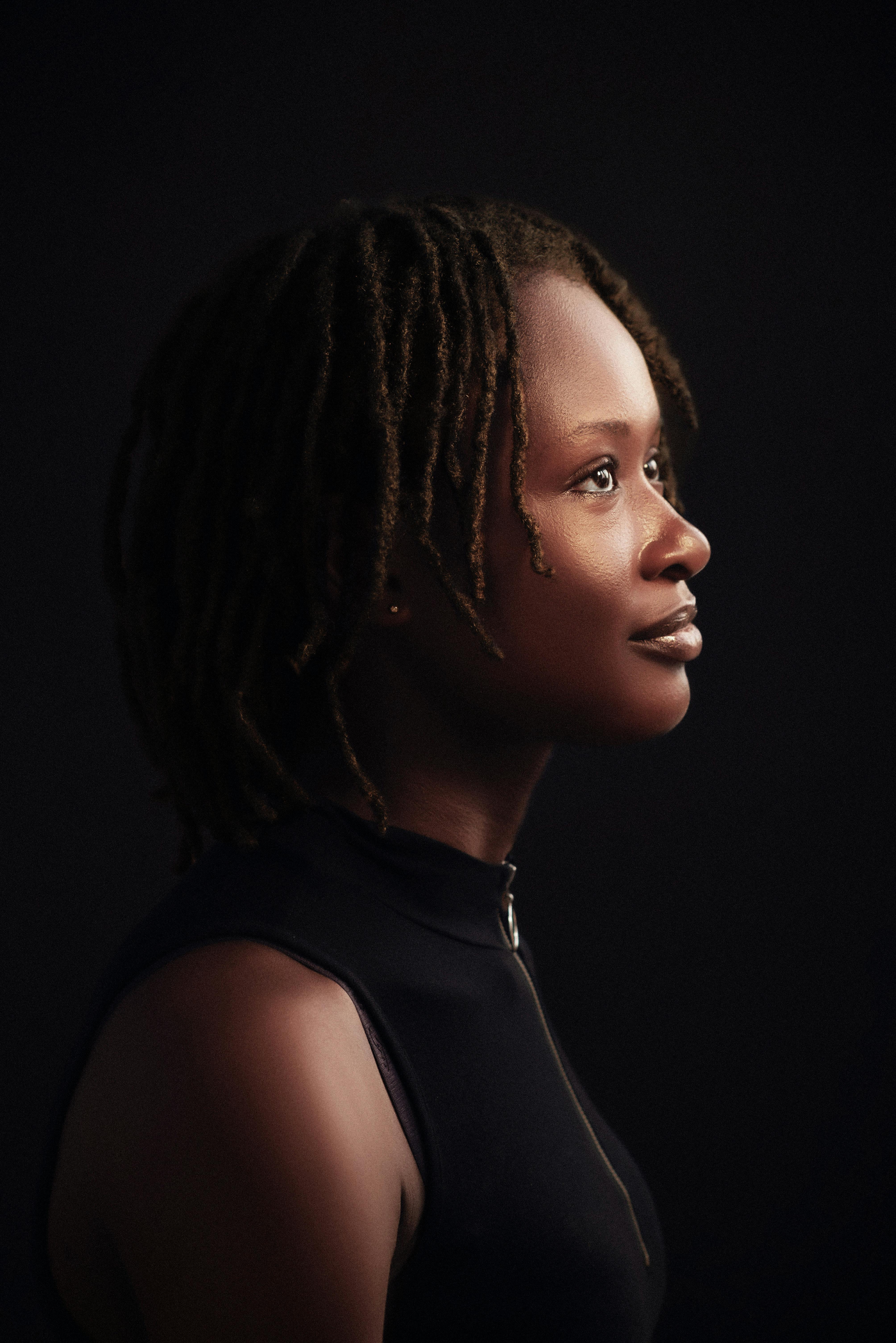 Artistic side profile portrait of a woman with dreadlocks against a dark background.