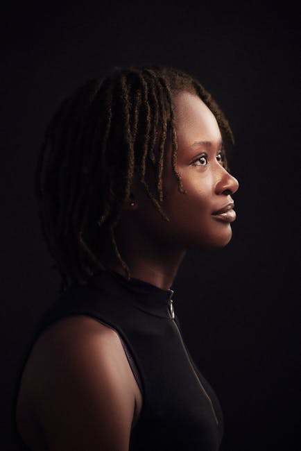 Artistic side profile portrait of a woman with dreadlocks against a dark background.