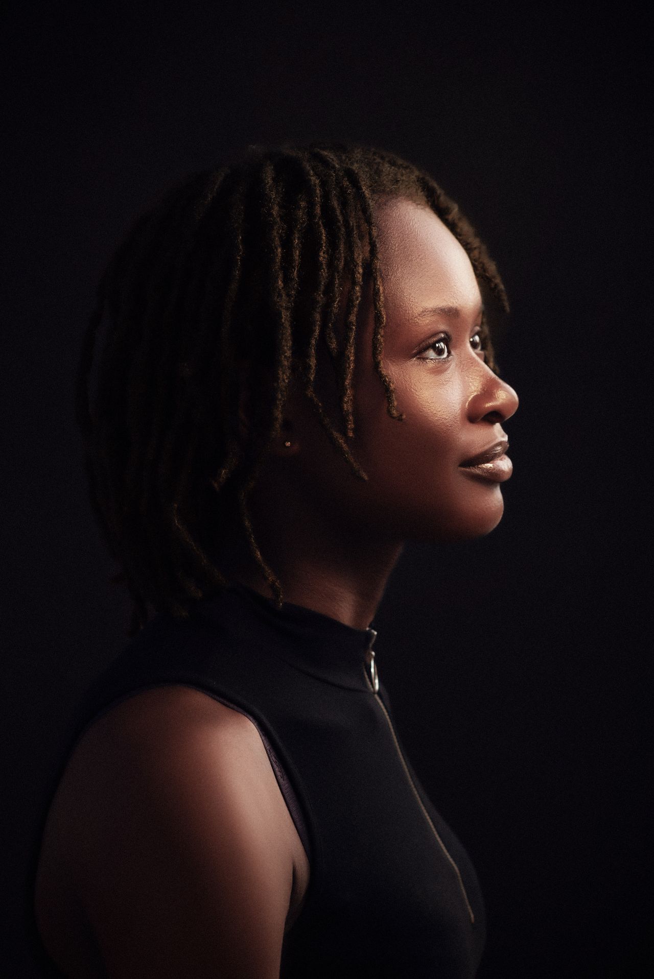 Artistic side profile portrait of a woman with dreadlocks against a dark background