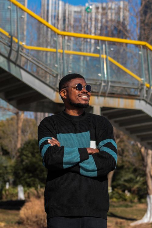 Free Man with sunglasses smiling confidently outdoors beneath a modern bridge. Stock Photo