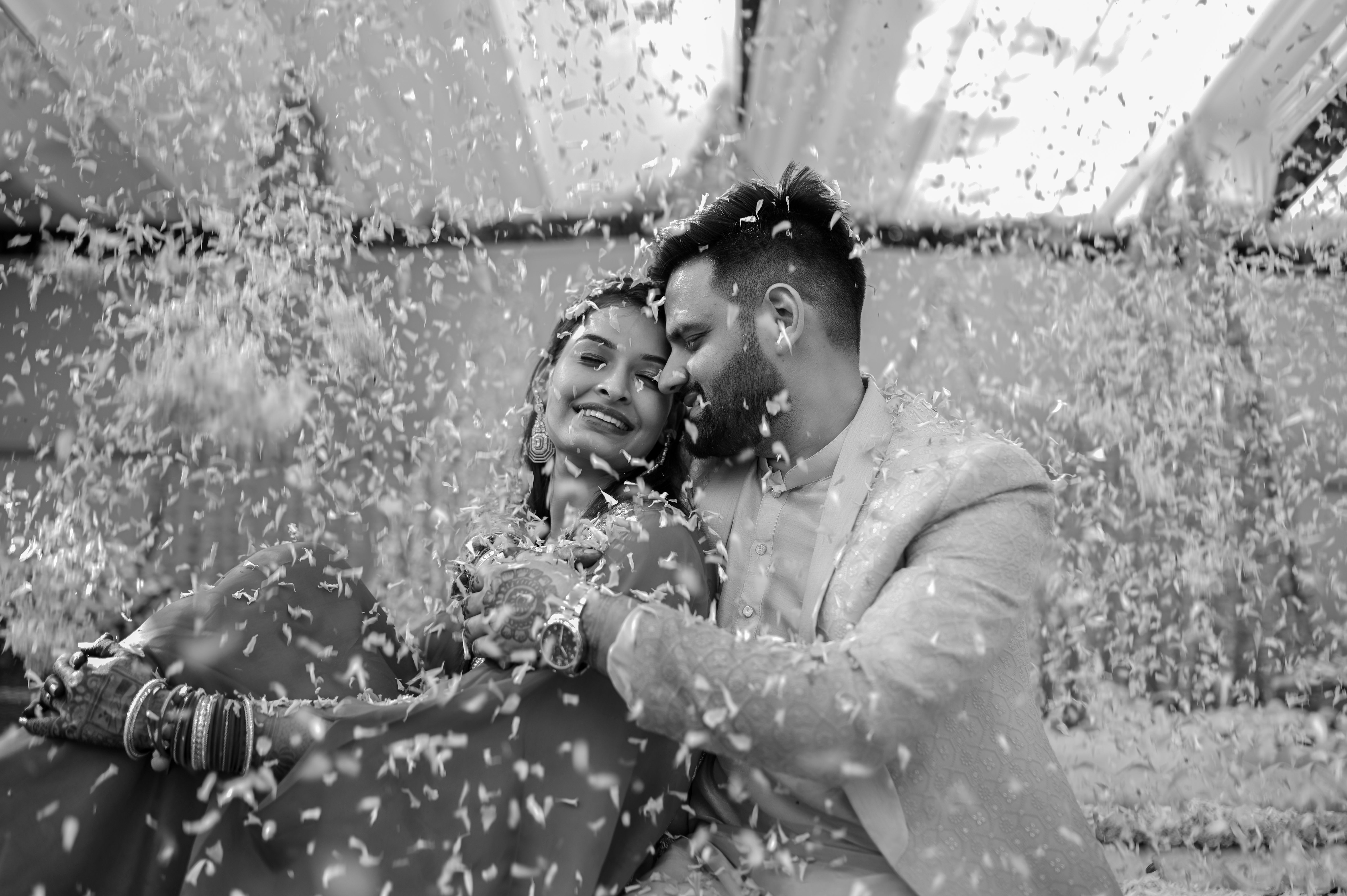 A joyous couple embraces amidst falling petals, capturing a special celebration moment.