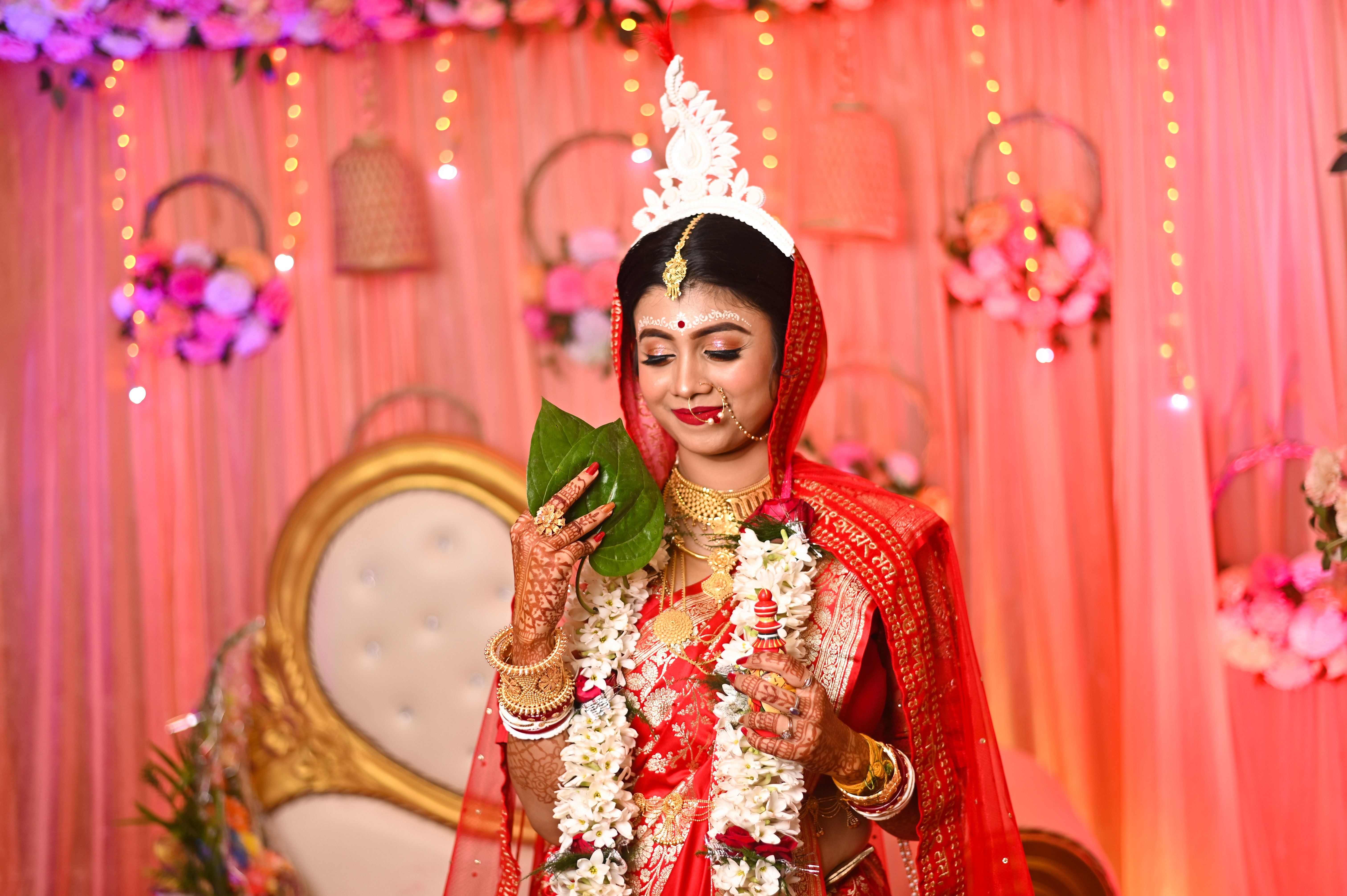 Bengali bride holding betel leaves, adorned with traditional jewelry and attire.