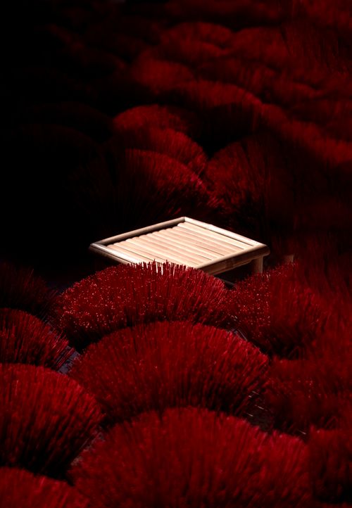 Free A striking scene of vibrant red incense sticks surrounding a bamboo table in low light. Stock Photo