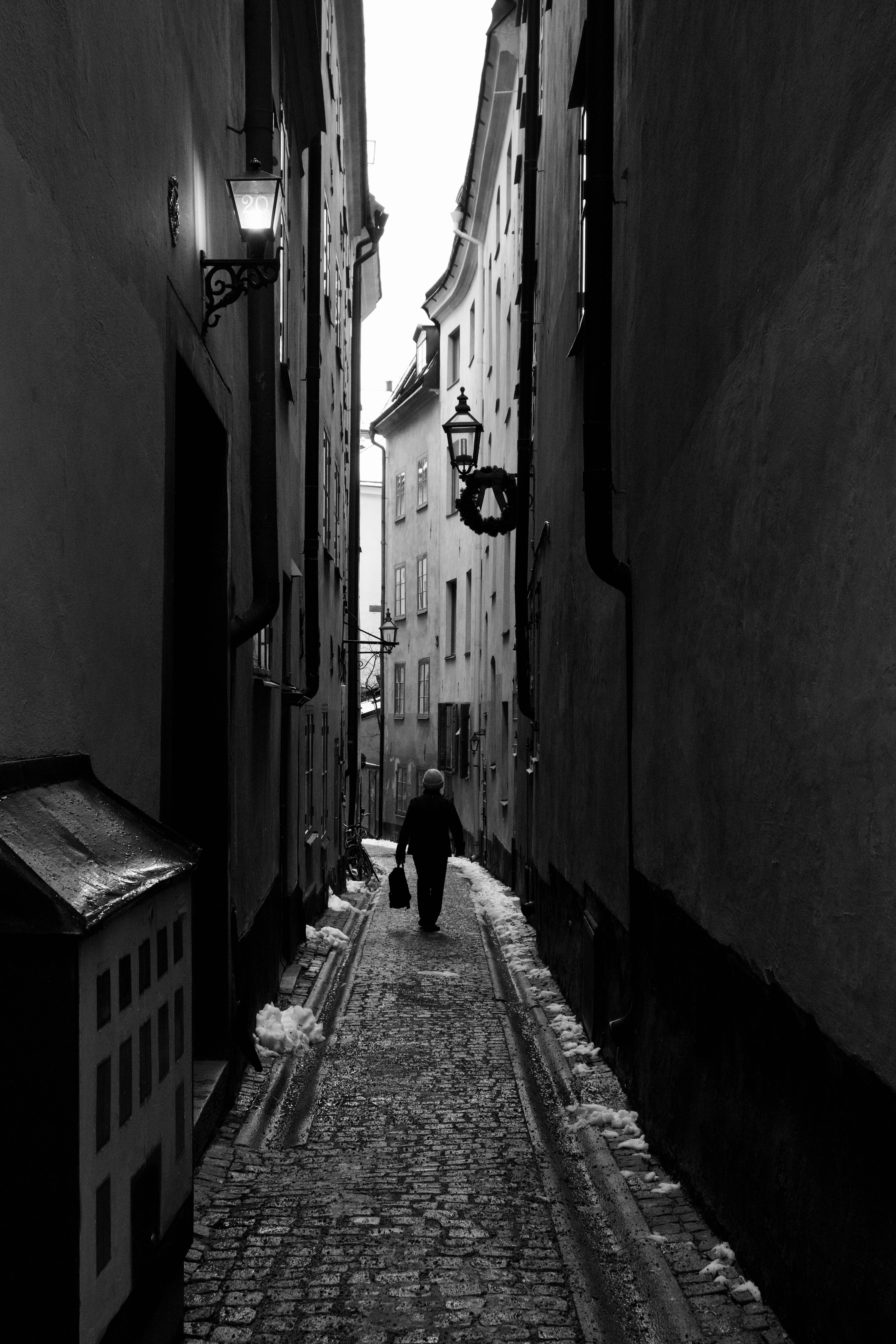 Black and white photo of a silhouette walking down a narrow street in Stockholm's Old Town.