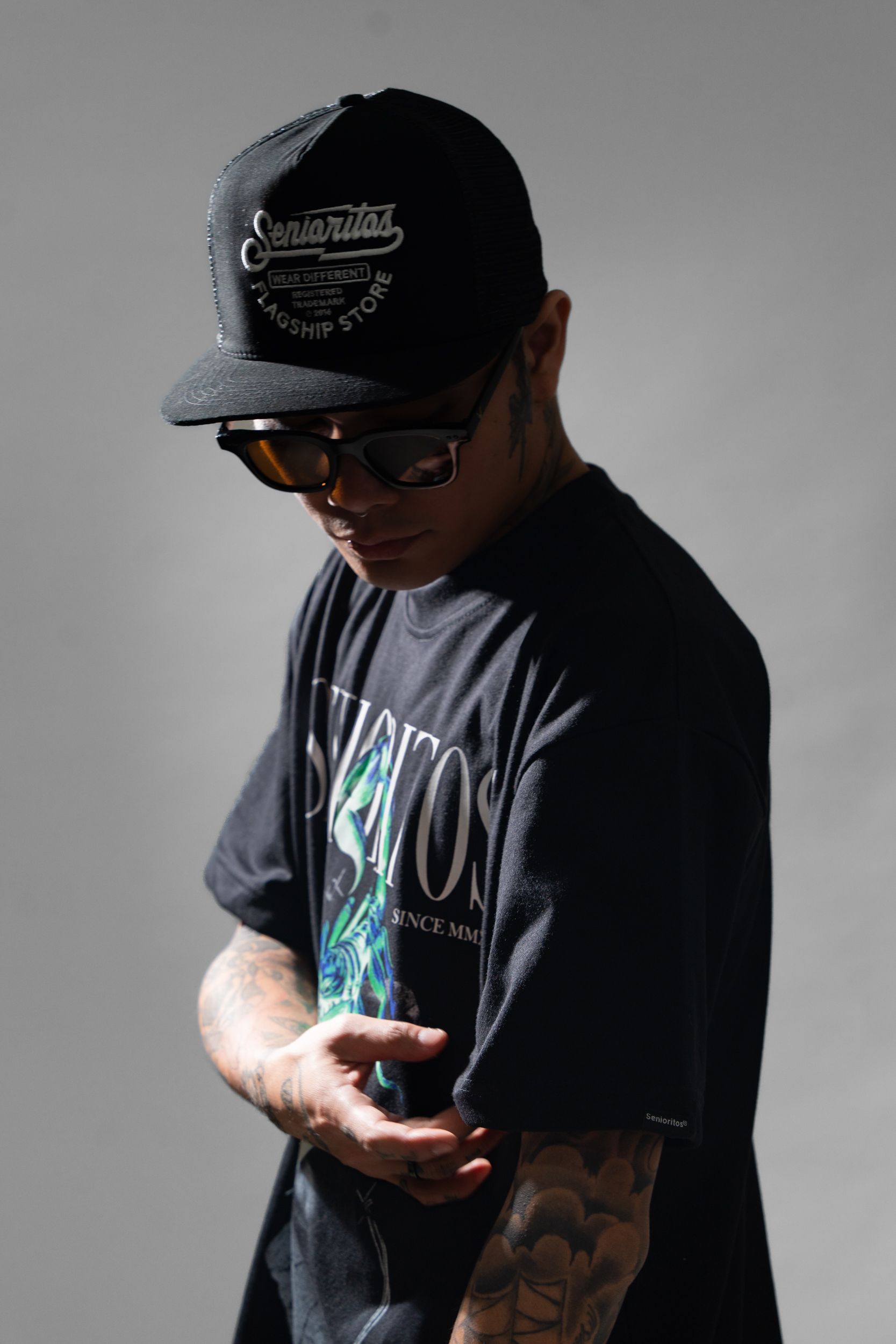 Portrait of a young man in casual clothing wearing a cap and sunglasses with tattoos.