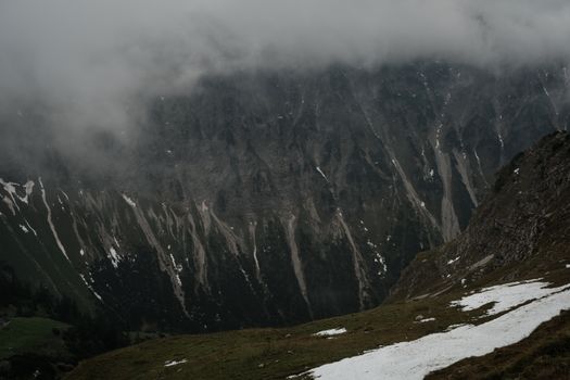 Misty mountain view with cliffs and scattered snow patches, creating a moody atmosphere.
