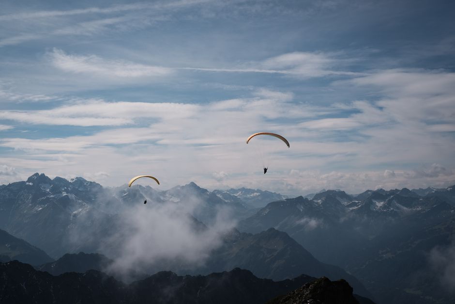Experience the thrill of paragliding above breathtaking mountain peaks with clear skies.