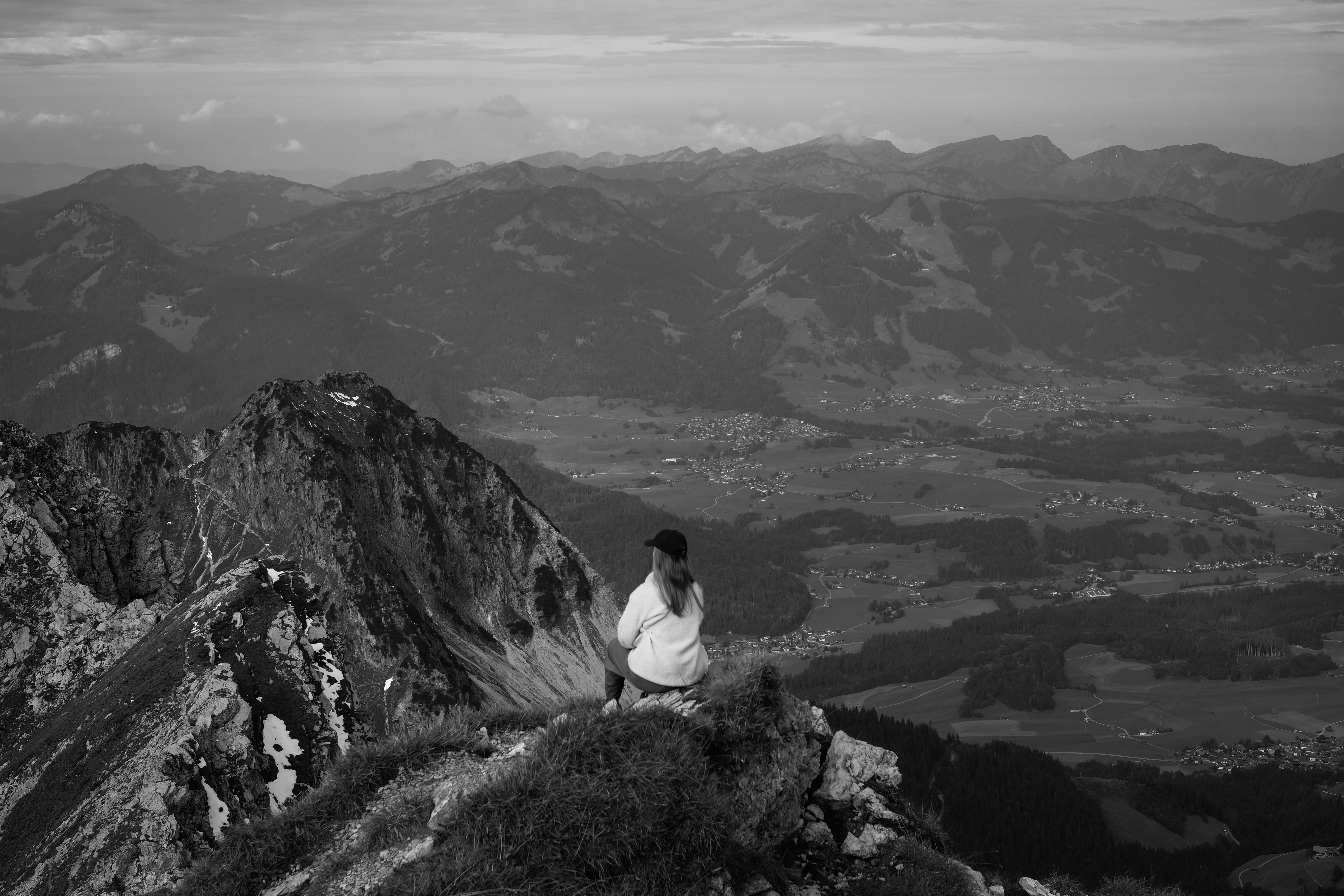 Black and white photo of a person overlooking a majestic mountain range in peaceful solitude.