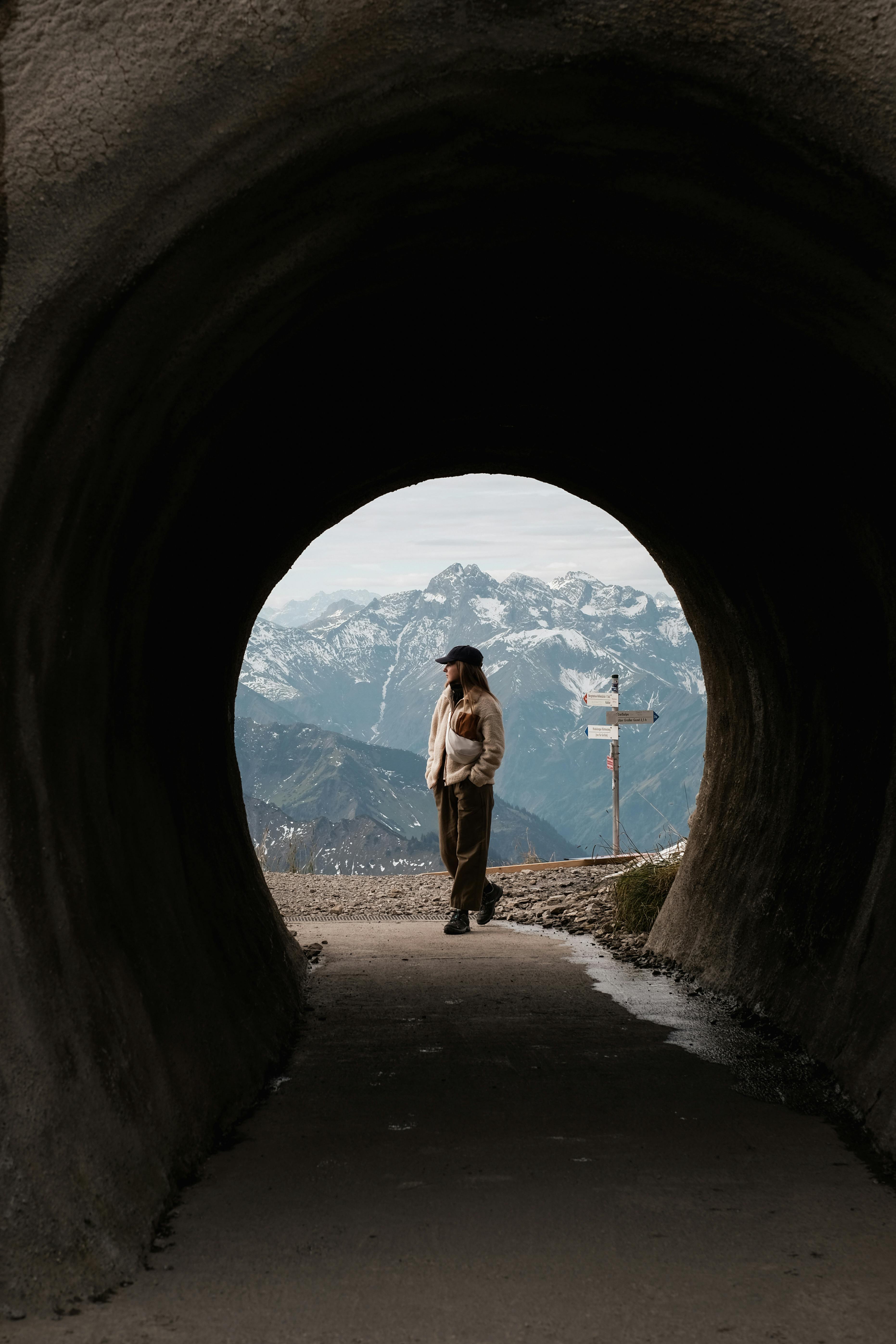 A person walks through a tunnel opening with a stunning view of snowcapped mountains in the background.