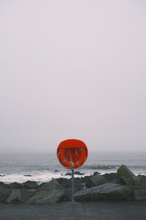 Free A solitary lifebuoy on a foggy beach, emphasizing safety and solitude. Stock Photo