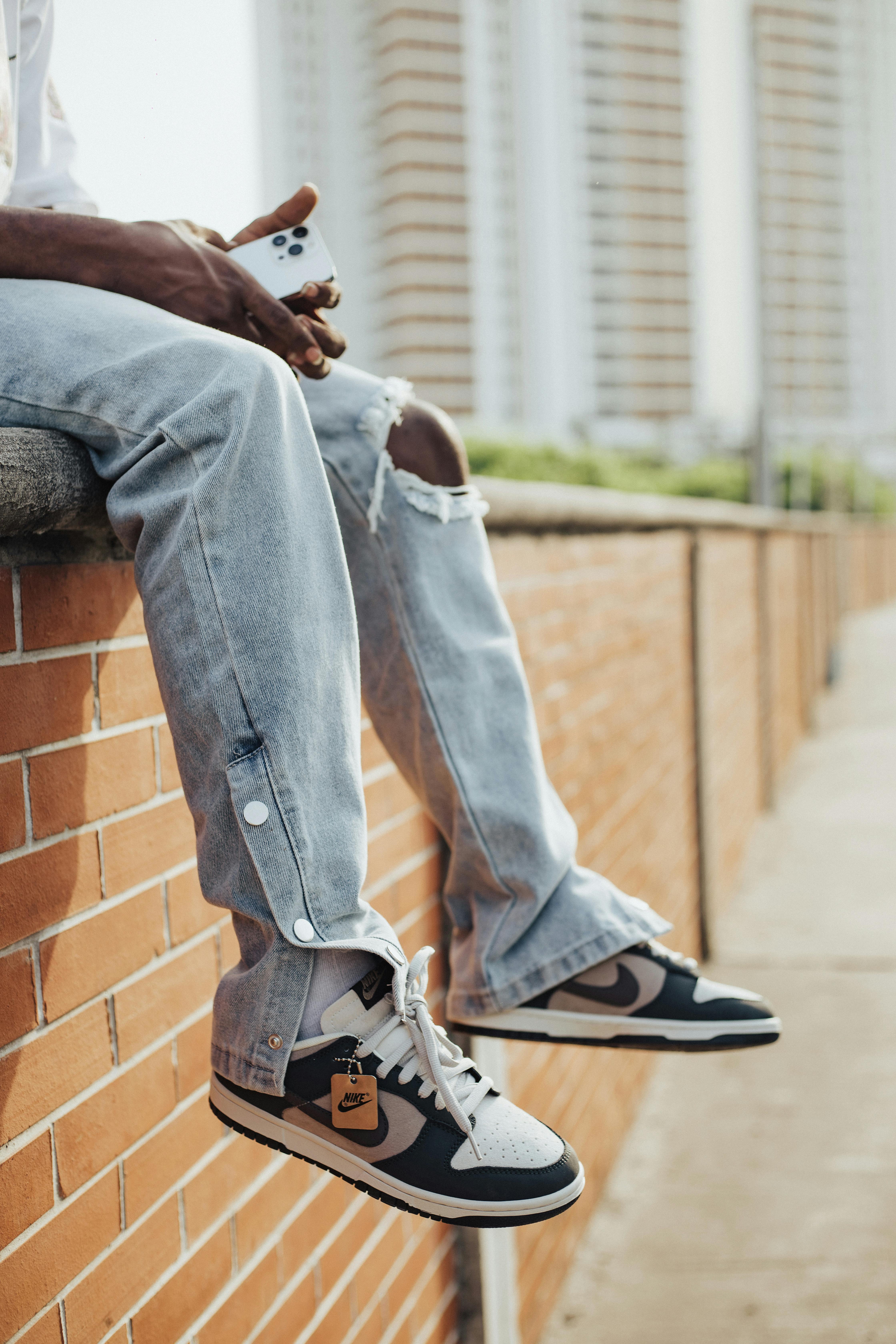 Stylish streetwear featuring torn jeans and sneakers on a brick wall.