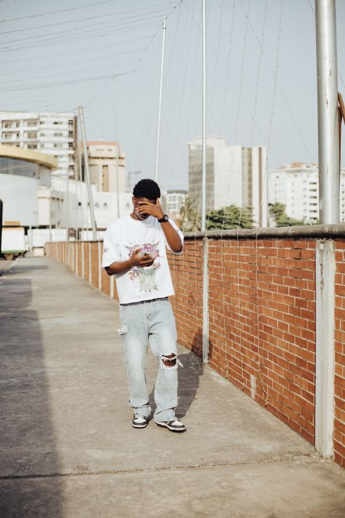 Free A young man in casual clothing walks on a city rooftop under bright daylight, showcasing urban fashion. Stock Photo