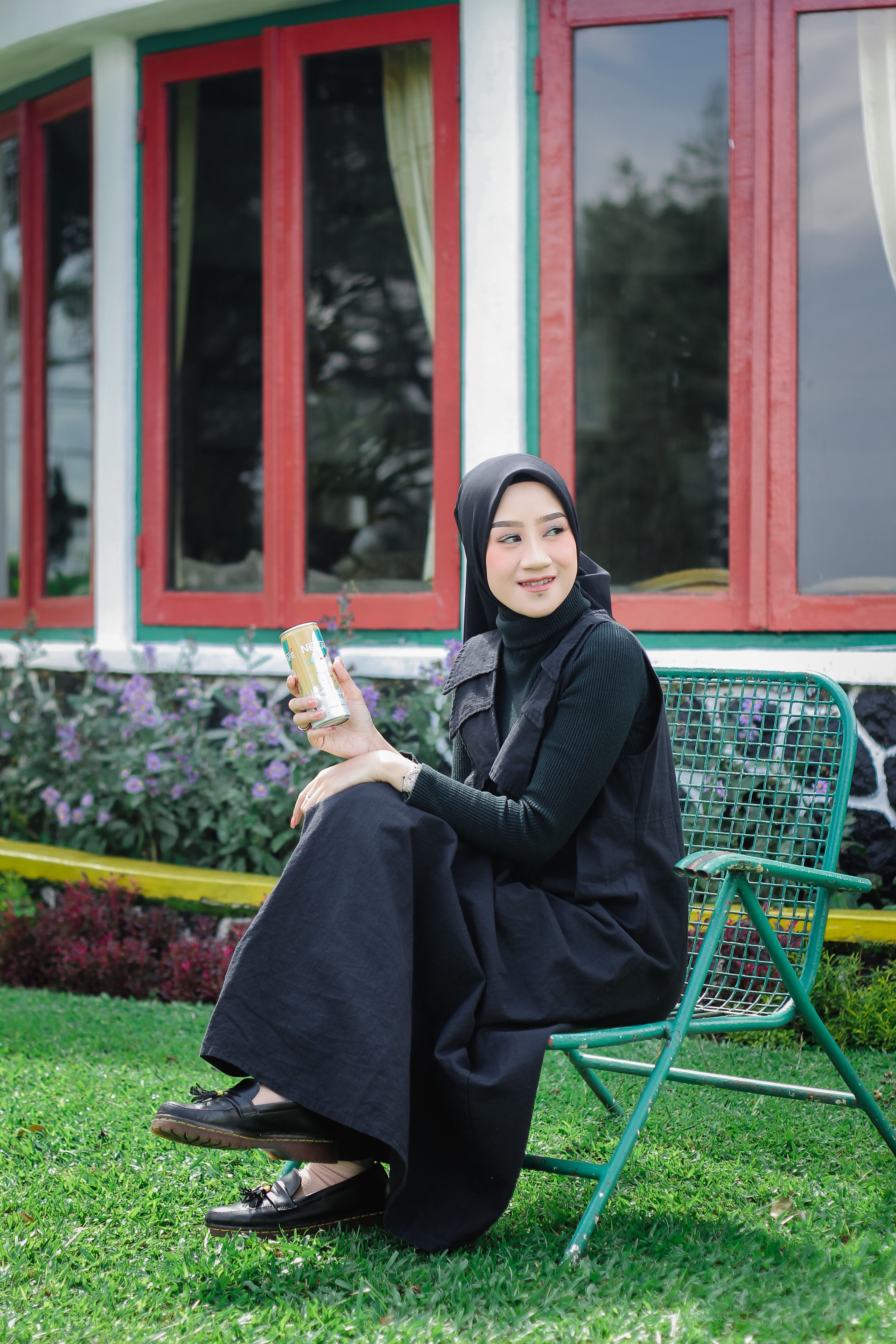 A young woman in a hijab relaxing on a chair outdoors, enjoying coffee.