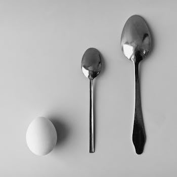 A minimalist still life featuring an egg and two spoons on a gray background.