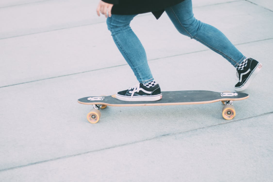 Persona Vestida Con Jeans Ajustados Azules Montando Longboard Negro