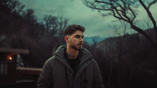 A dramatic outdoor portrait of a man in a winter coat against a moody Kurdish landscape.