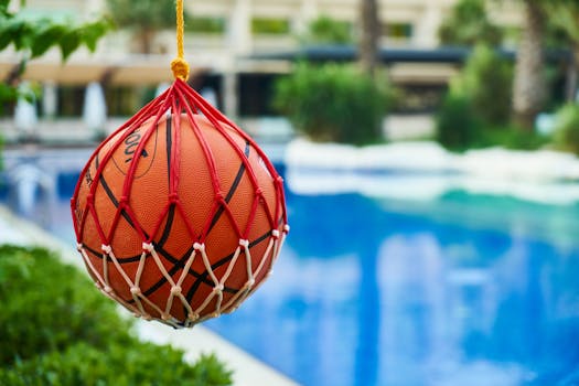 A vibrant basketball suspended in a net by a poolside at a tropical resort, evoking leisure and summer vibes.