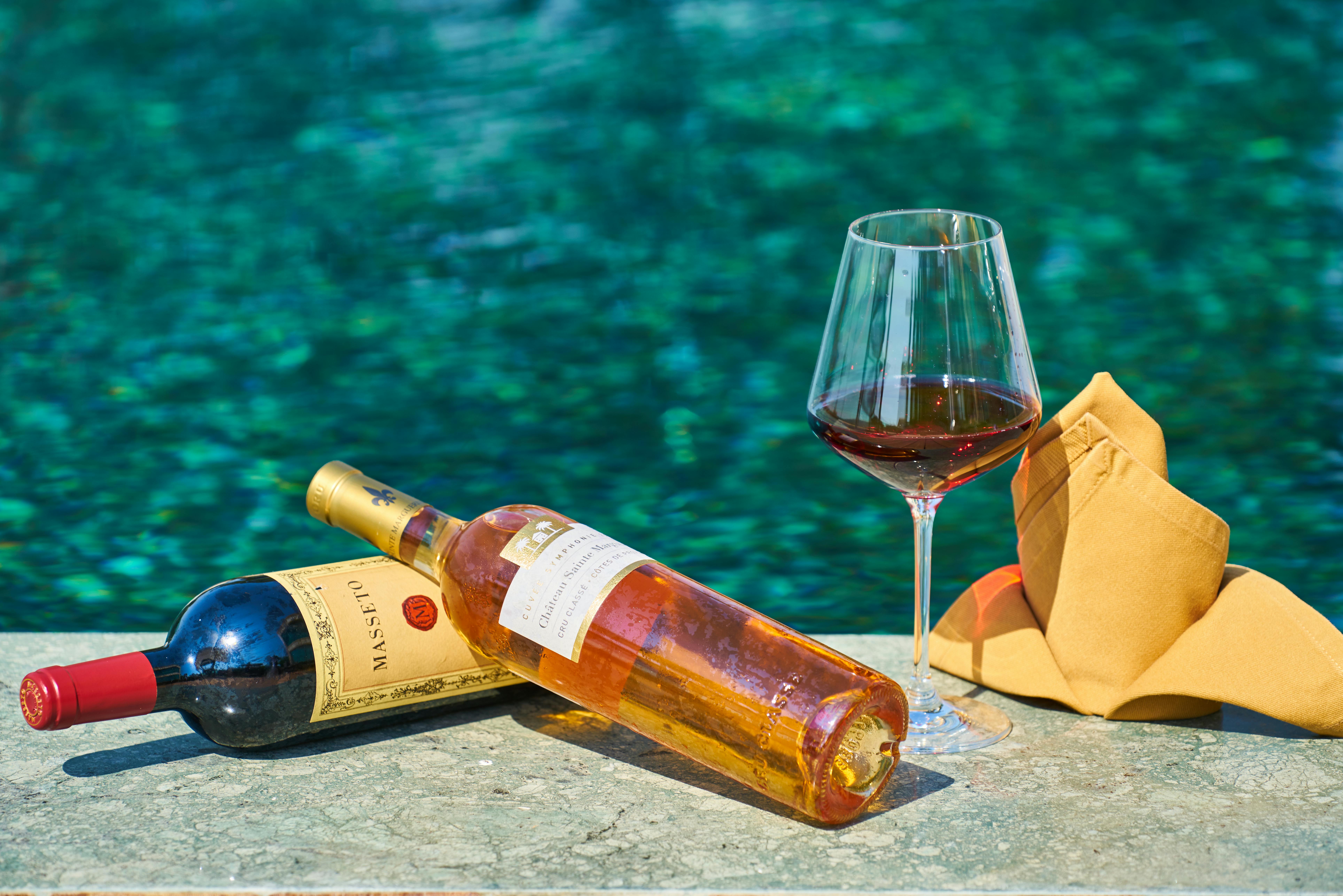 two labeled bottles of wine beside a wine glass by the pool