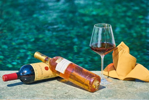 Deux Bouteilles De Vin étiquetées à Côté D'un Verre à Vin Au Bord De La Piscine