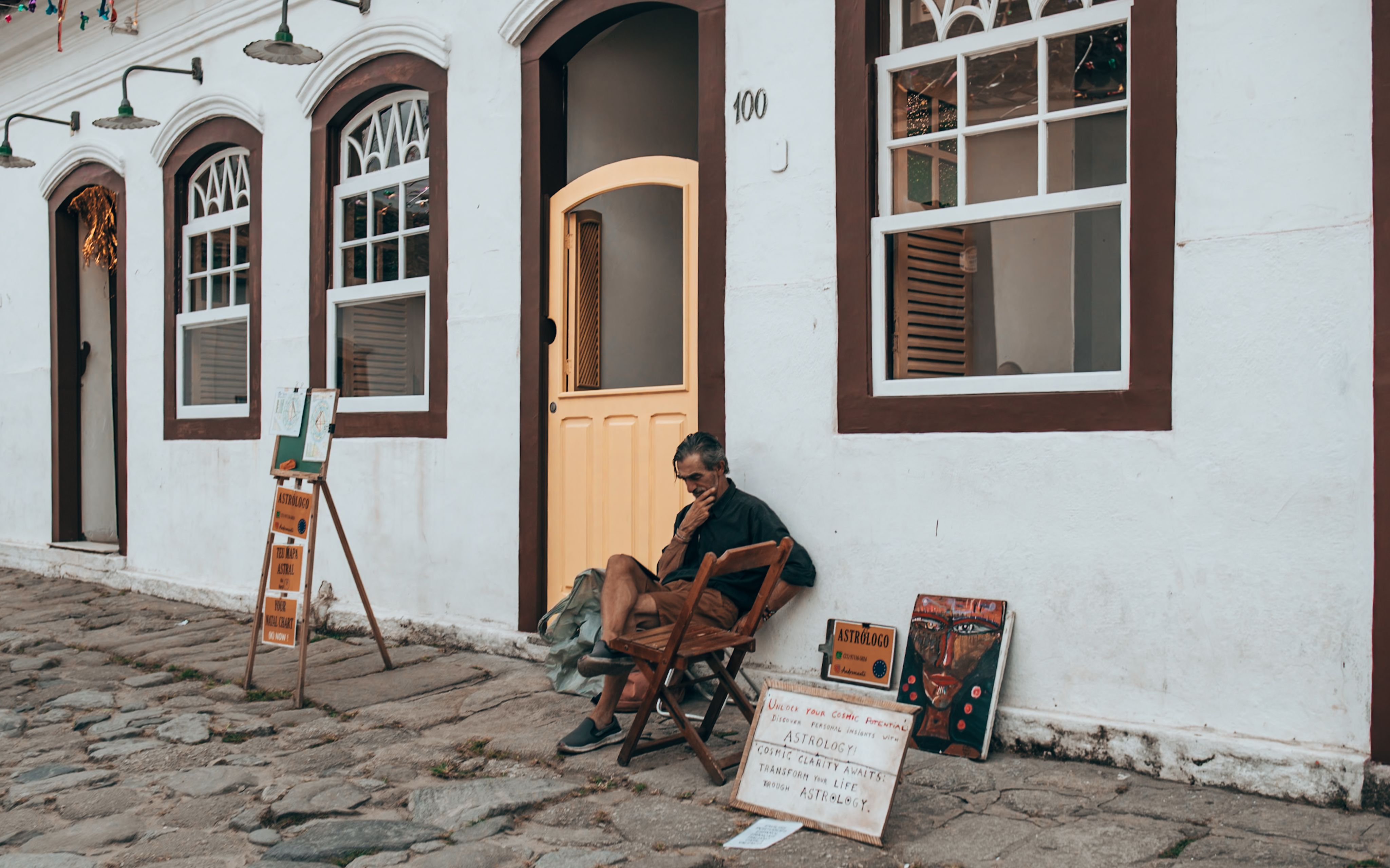An elderly man sits reading outside a charming, historical building.