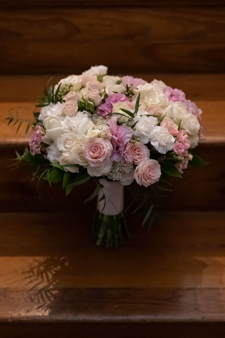 A beautiful bridal bouquet featuring white and pink roses elegantly placed on wooden stairs.
