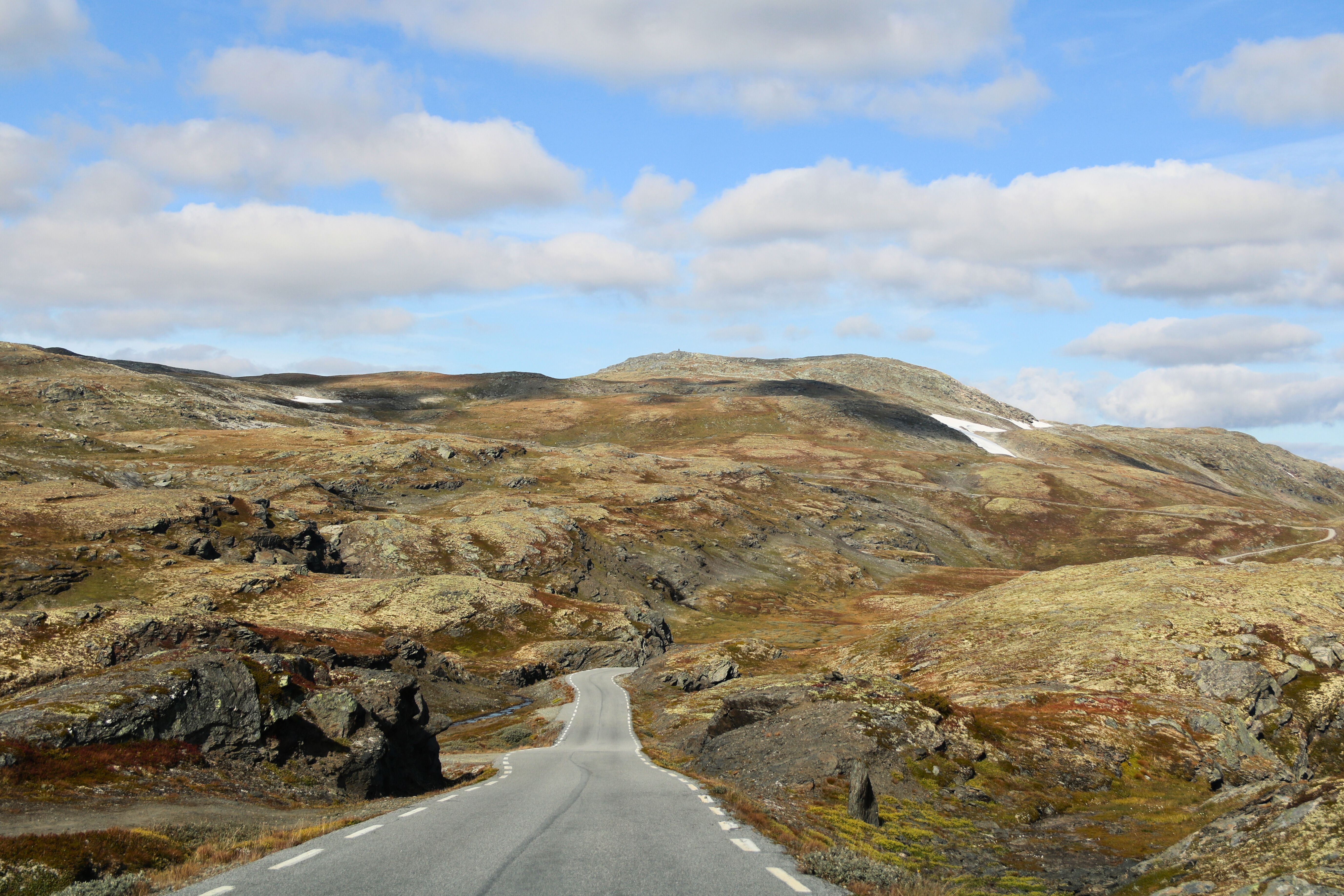 A serene landscape with a winding road through the rugged mountains of Norway under a bright sky.