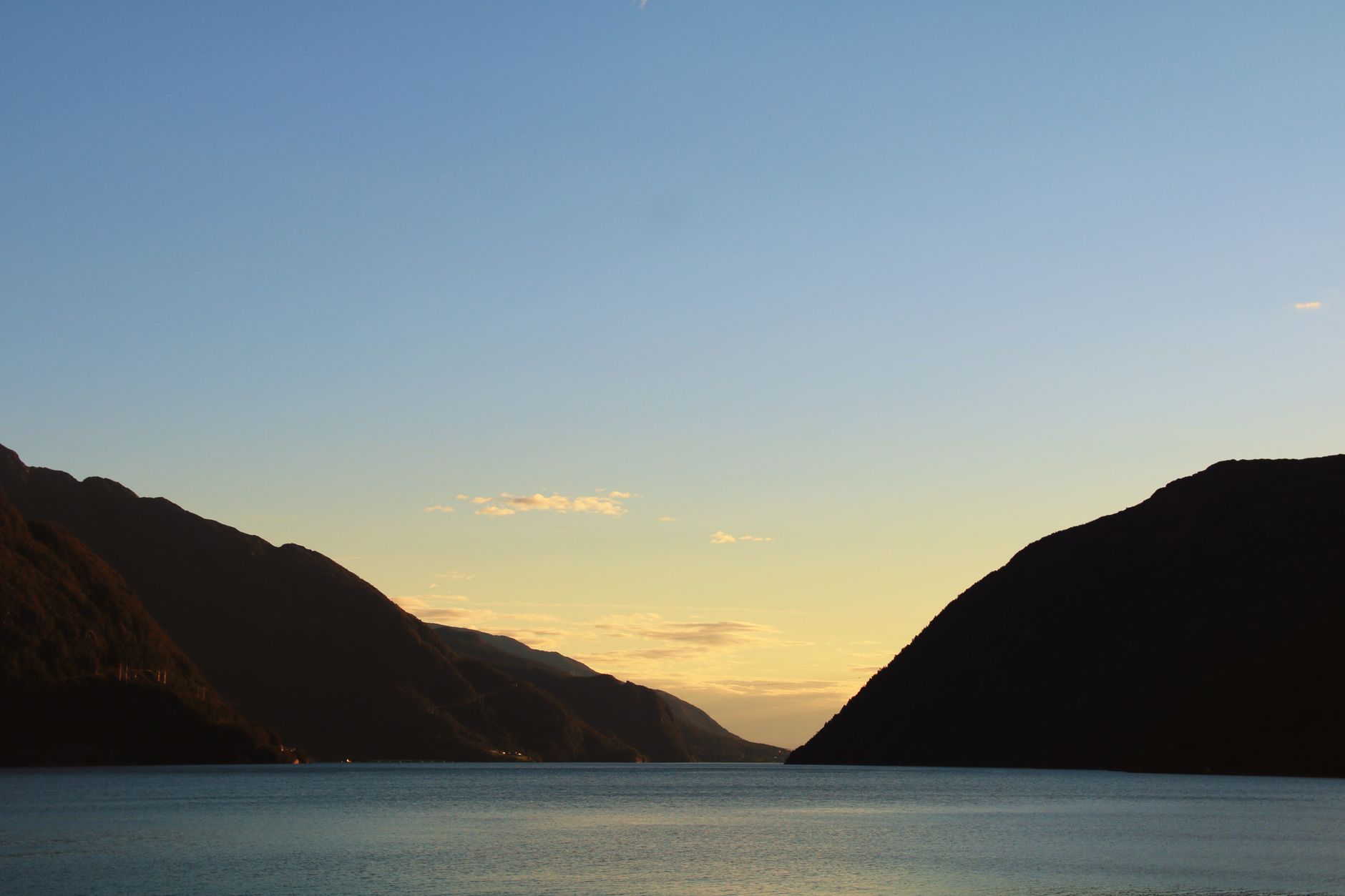 Beautiful sunset view over a Norwegian fjord with calm waters and silhouetted hills.