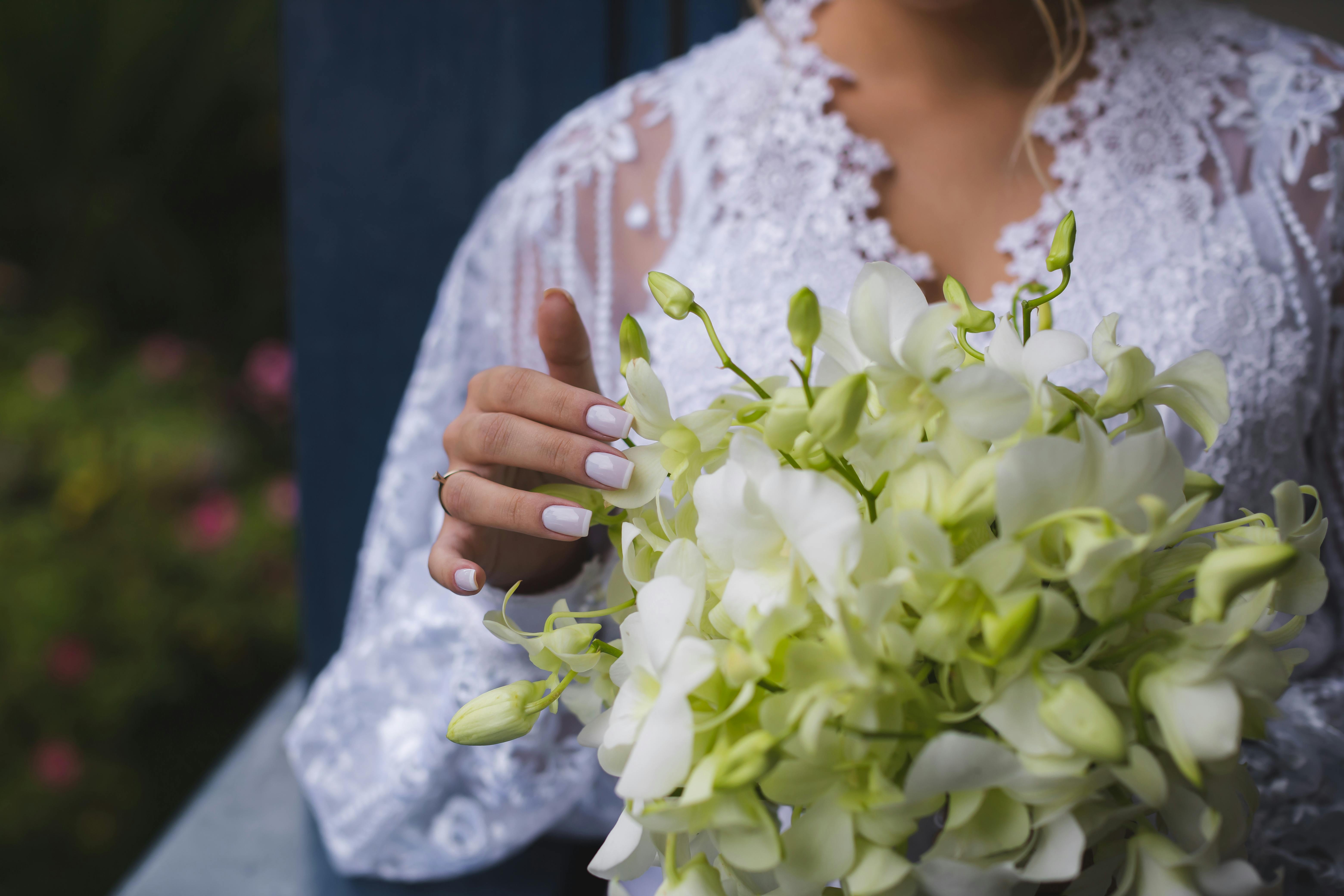 Close-up of bride holding white orchid bouquet, highlighting elegant wedding details.