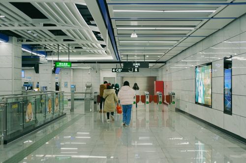 Free Passengers walk through a modern subway station hallway with electronic billboards and turnstiles. Stock Photo
