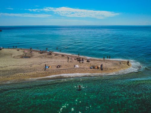 Free Vibrant aerial capture of people enjoying a sunny day on a sandy beach by the clear sea. Stock Photo