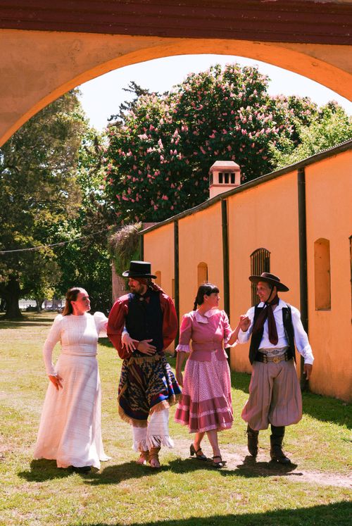 Free A group of four adults wearing traditional costumes walk joyfully under a yellow arch. Stock Photo