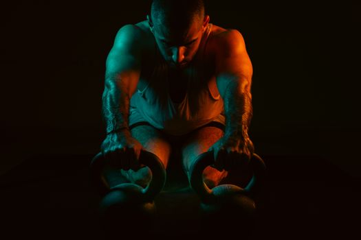 A strong man intensely working out with kettlebells in a dark gym setting.