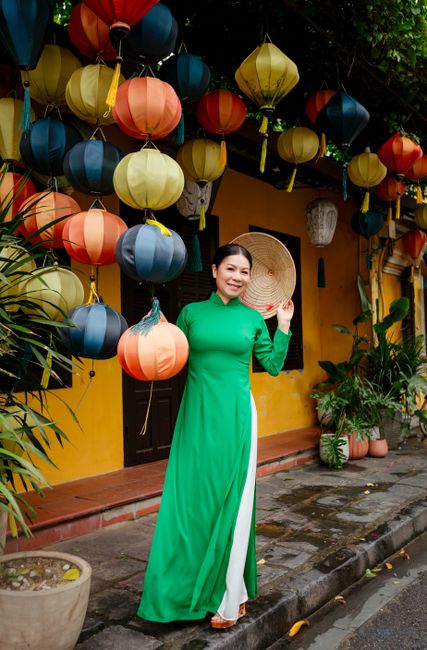 Woman in green ao dai posing by colorful lanterns in Hội An, Vietnam.