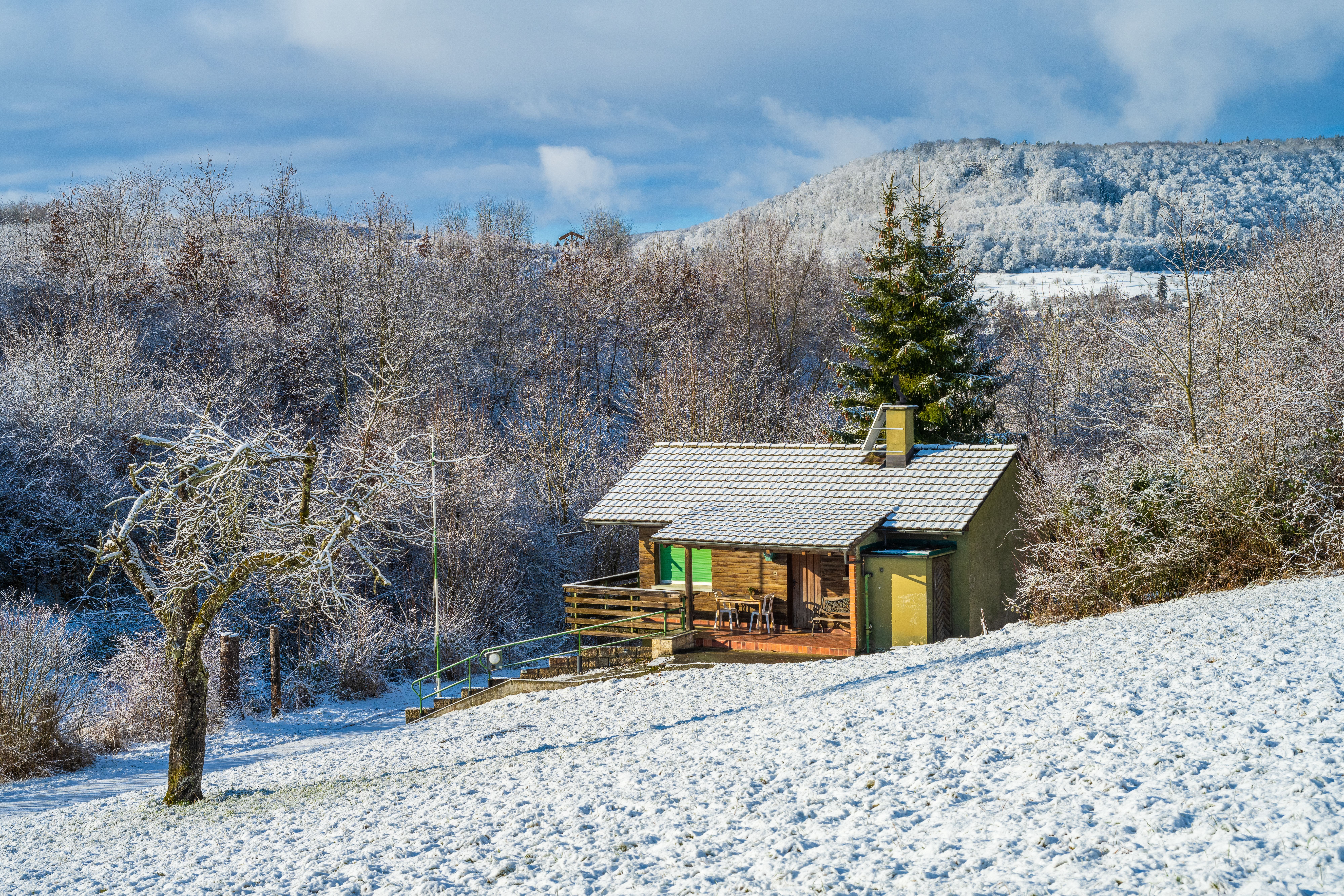 Une cabane en bois nichée dans un paysage hivernal enneigé avec des arbres nus et des montagnes.