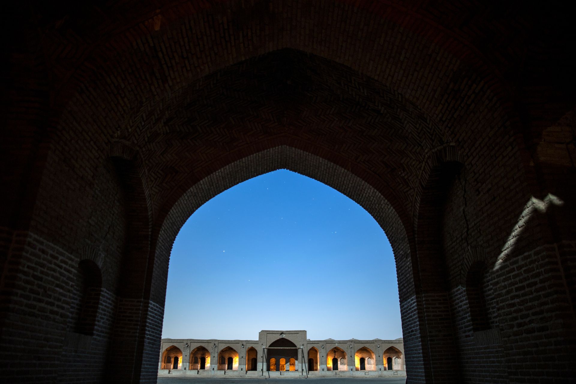 Majestic archway framing traditional Iranian architecture in Qom Province during twilight.