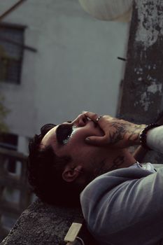 Moody portrait of a tattooed man with eye makeup in an urban setting.