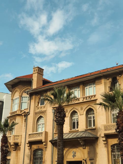 Free Elegant Mediterranean-style architecture with palm trees under a sunny sky. Stock Photo