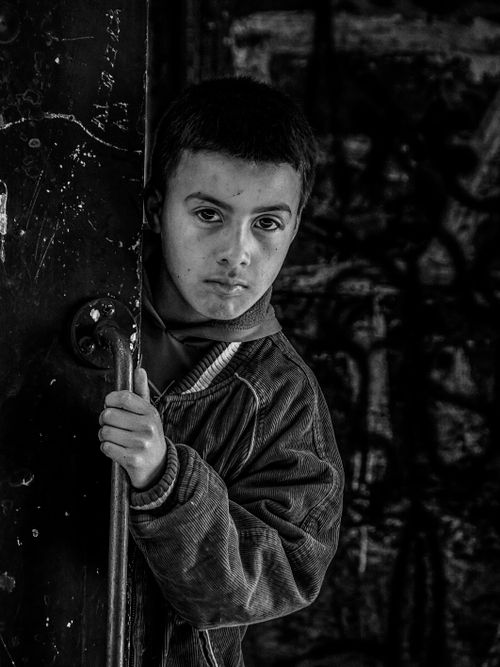 Free A young boy peers from a doorway against a graffiti-covered urban backdrop. Stock Photo