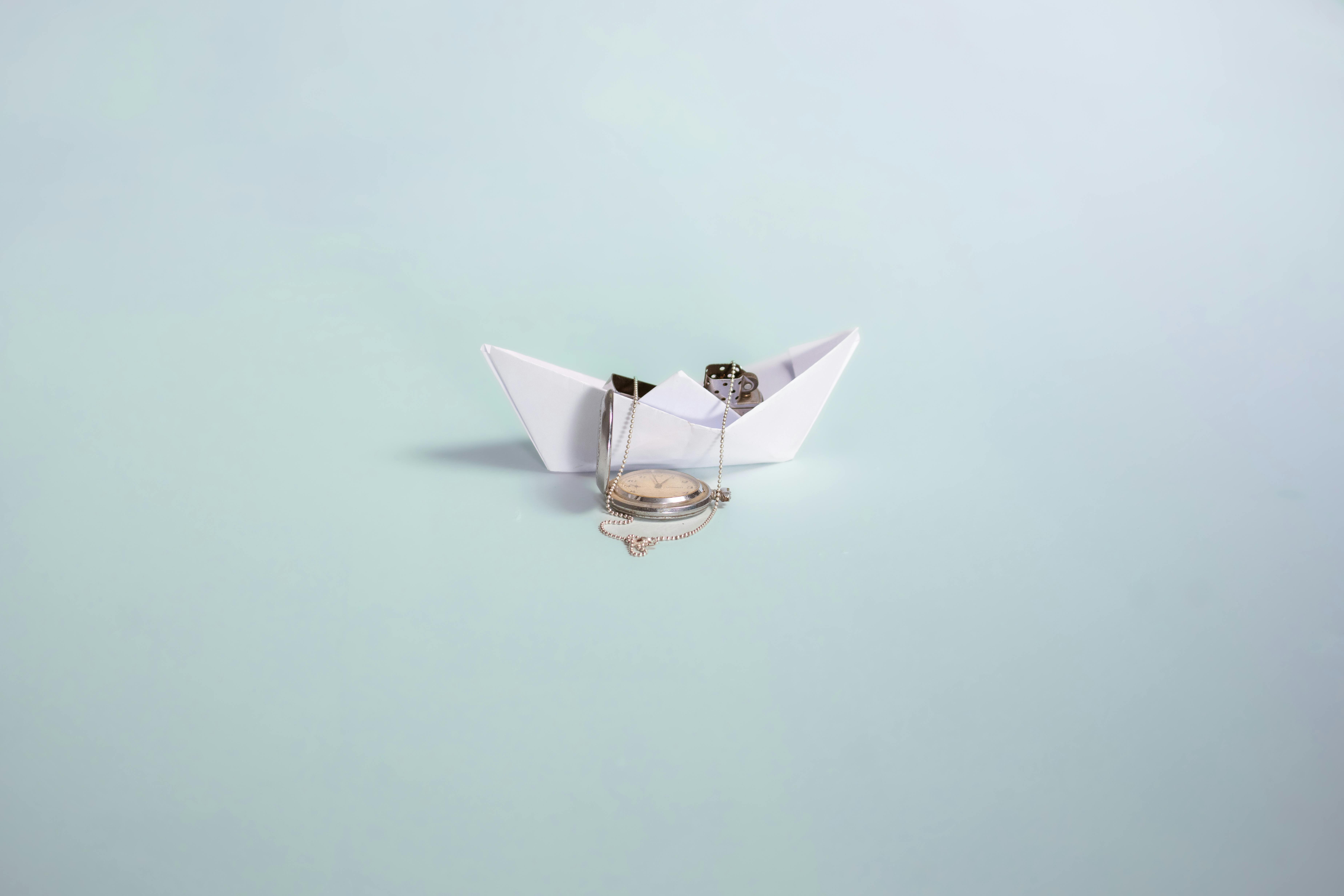 bezplatná Jednoduchá a kreativní kompozice papírové lodičky a historických kapesních hodinek na pastelovém pozadí. Základová fotografie